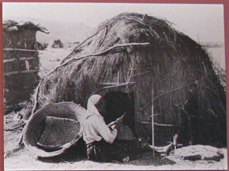 IMG_9897 -grasshut.JPG - Worn baskets were not thrown away, they were mended by skilled hands to provide more years of use. This woman sits in front of her brush house--not unlike houses built by the Hohokam, next to a wattle and daub structure